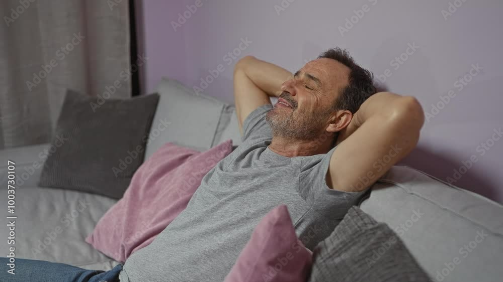 Middle-aged man relaxing indoors on a couch, with a content expression and arms behind his head in a cozy living room setting with pillows. Middle-aged man relaxing indoors on a couch, with a content expression and arms behind his head in a cozy living room setting with pillows.