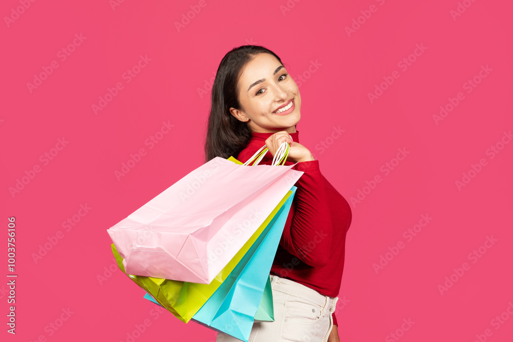 A young woman beams with joy, showcasing vibrant shopping bags in various colors. The playful pink background enhances her excitement, capturing the essence of a fun shopping experience. A young woman beams with joy, showcasing vibrant shopping bags in various colors. The playful pink background enhances her excitement, capturing the essence of a fun shopping experience.