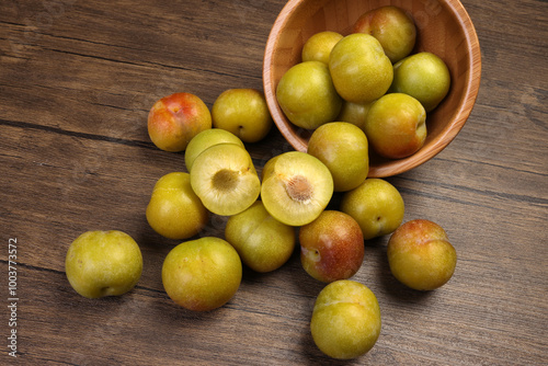 Ripe sweet small mini plum green maroon on rustic wooden table bowl black background photo