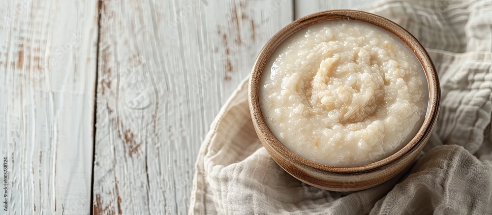 Nutritious breakfast porridge for children A bowl of baby food placed on fabric against a white wooden background The idea of healthy eating and proper nutrition Copyspace close up