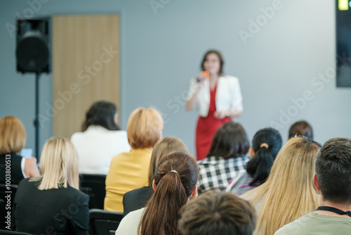 A woman presenting to a business audience in a conference room. Attendees sitting and listening attentively.