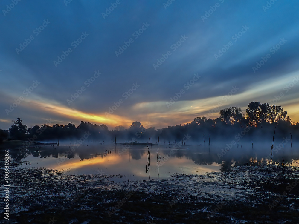 Fototapeta premium Sky colors at sunrise with sun rays in the morning fog over the water