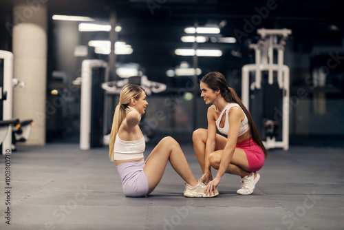 Side view of fit sportswoman doing crunches in a gym while her coach is helping her.