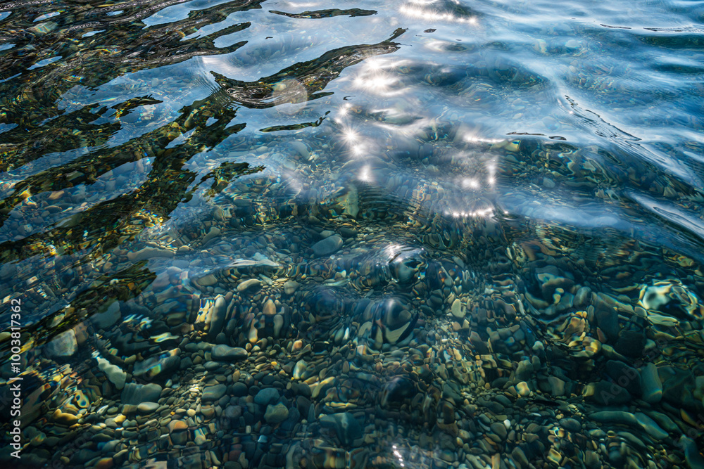 Underwater pebble backgrounds. Colorful stones sea bottom and sea fish in the sun rays. View from above through clear water. Seascape wallpaper texture.
