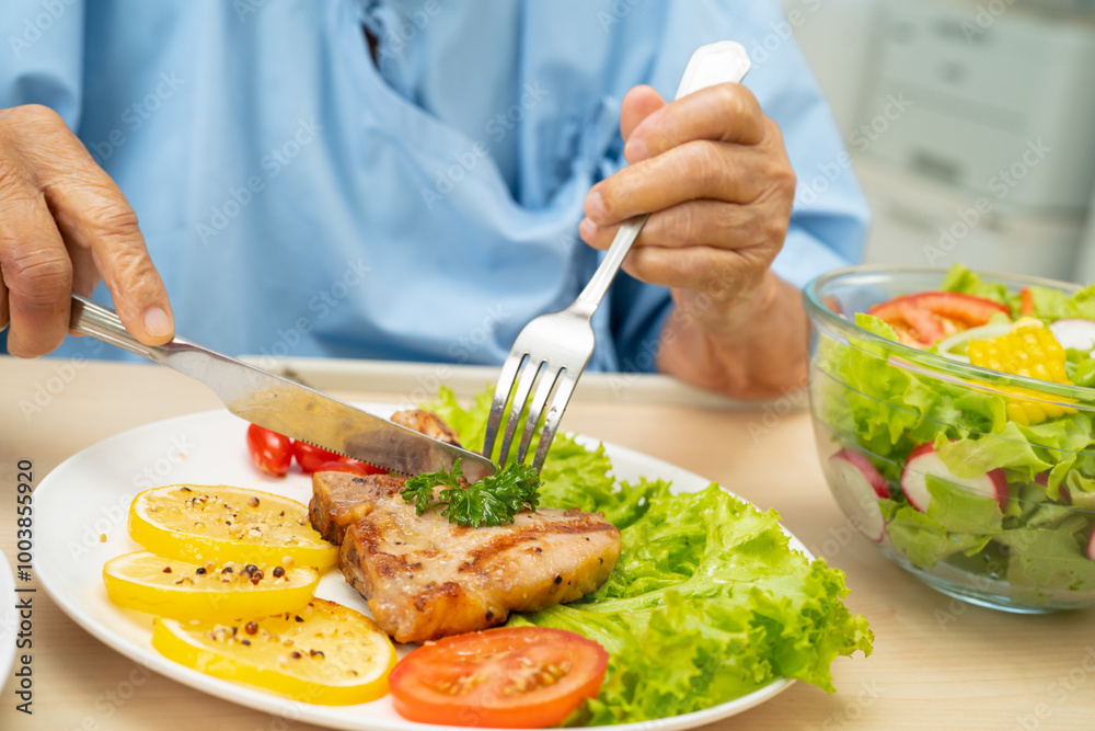 Asian senior woman patient eating pork chop stake and vegetable salad for healthy food in hospital. Asian senior woman patient eating pork chop stake and vegetable salad for healthy food in hospital.