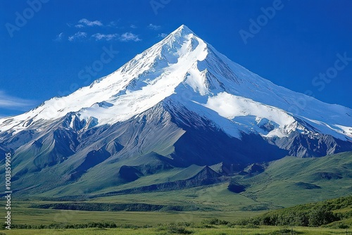 A majestic snow-capped mountain peak rises against a clear blue sky, with rolling green hills in the foreground.