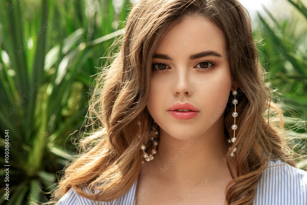 Young beautiful woman with perfect skin and big pearl earrings and curly hair front of greens plants. Close up, selective focus.