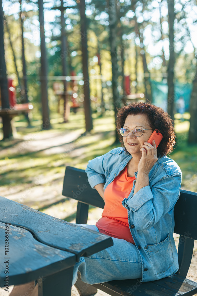 The elderly woman holding her mobile phone to her ear while sitting on a park bench The elderly woman holding her mobile phone to her ear while sitting on a park bench