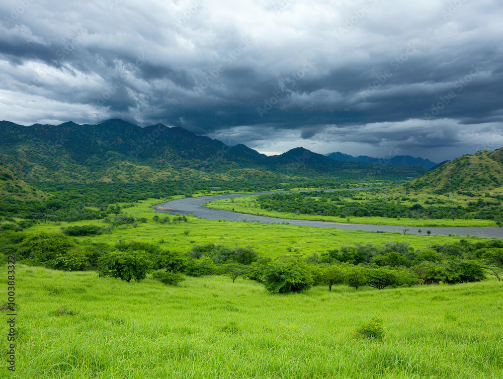 A river winds through a vibrant green valley under dark, stormy skies. The looming clouds promise heavy rain, contrasting with the serene landscape of lush fields and distant mountains.