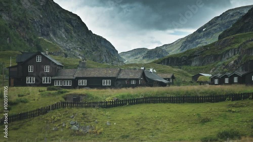 Traditional wooden buildings sit in a green Boverdalen valley, surrounded by towering mountains and rocky slopes. photo