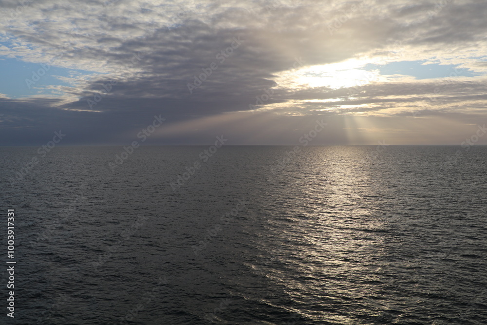 Fototapeta premium seascape with a cloudy sky and the sun breaking through a hole in the sky