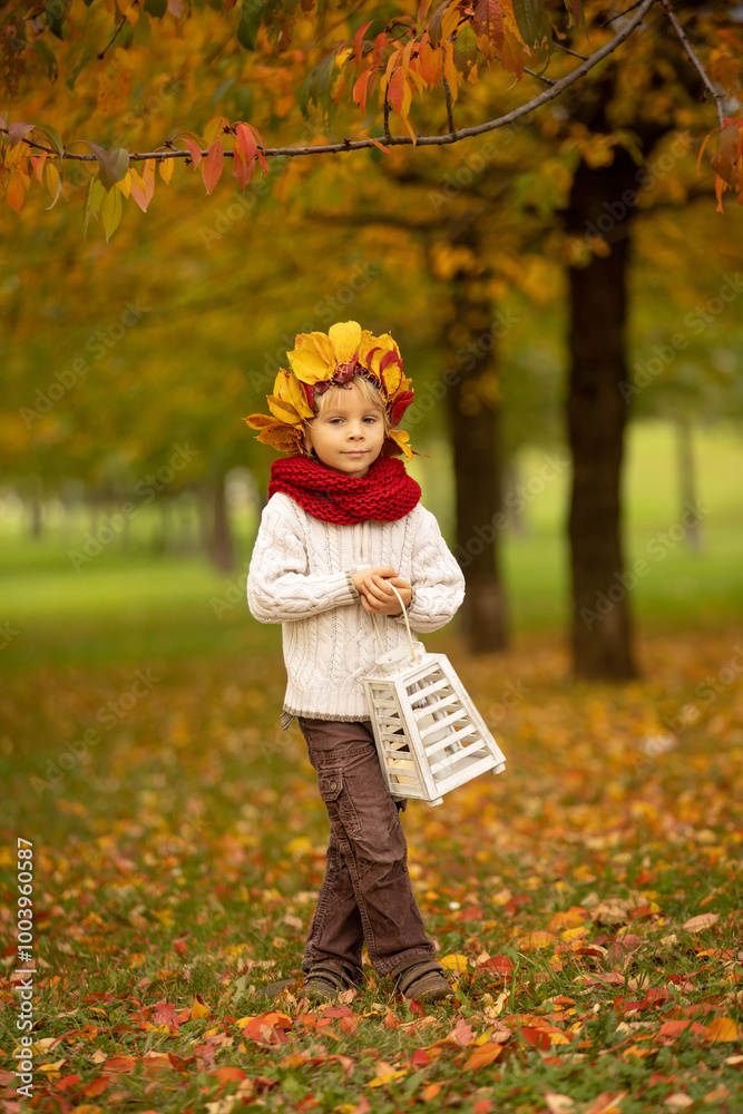 Adorable little child, blond boy with crown from leaves in park on autumn day.