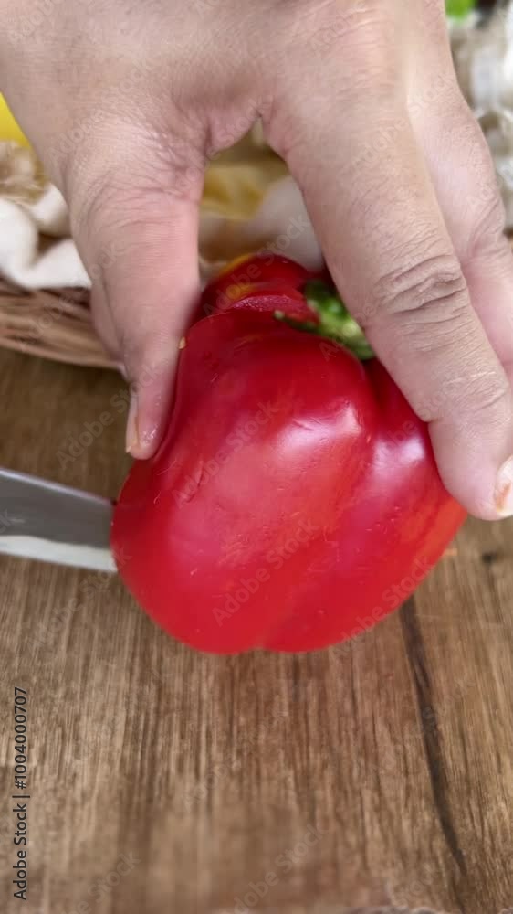 Cutting of a red capsicum with knife on a wooden chopping board. Cutting of a red capsicum with knife on a wooden chopping board.