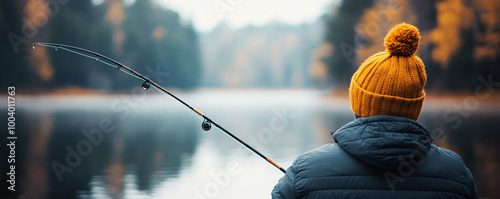 Person fishing by calm lake, wearing a yellow hat, surrounded by autumn foliage. photo