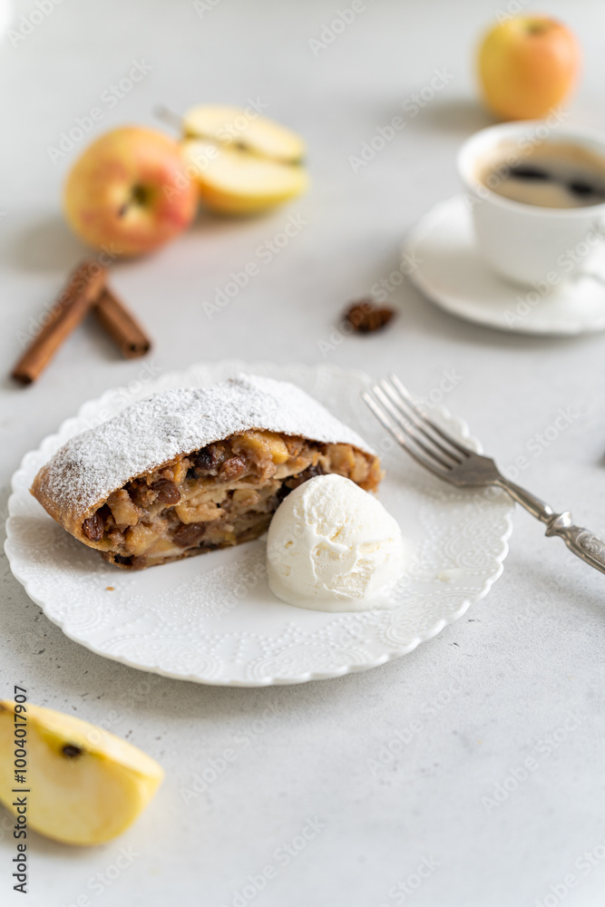 Freshly baked powdered apple strudel with raisins and ice cream on white plate with red apples and cinnamon on white background. homemade Apfelstrudel, austrian germany cuisine. Menu, recipe, close up Freshly baked powdered apple strudel with raisins and ice cream on white plate with red apples and cinnamon on white background. homemade Apfelstrudel, austrian germany cuisine. Menu, recipe, close up