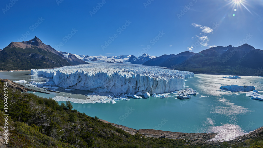 Fototapeta premium Perito Moreno Glacier in Patagonia, Argentina, captured at noon. The bright sunlight illuminates the vast expanse of ice, highlighting its majestic beauty against the clear blue sky.