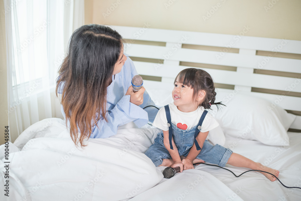 Obraz premium Happy Asian family loving children, kid and her sister holding microphone and singing together on bed in bedroom