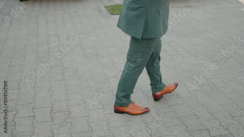 Man in a green suit walking on a cobblestone path, wearing brown shoes photo