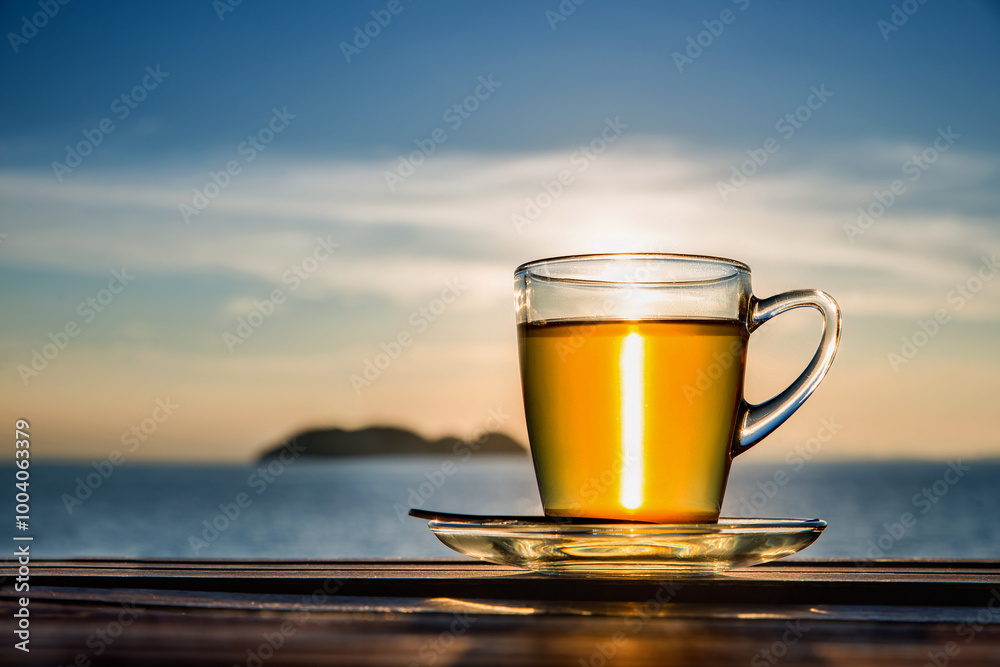 Cup of amber green tea on wooden tabletop shining in the sunset light. Sea view. Cup of amber green tea on wooden tabletop shining in the sunset light. Sea view.