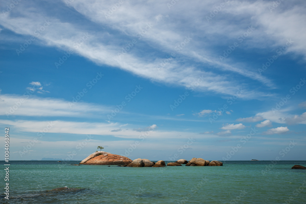 Fototapeta premium Big rock on the seashore front of the small tropical rock island with lone tree. Ocean view.