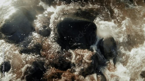 wet round pebbles on rocky beach washed by rampant ocean waves on sunny day photo