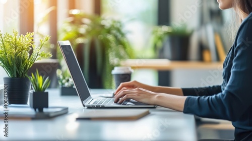 A person typing on a laptop in a bright, plant-filled workspace.