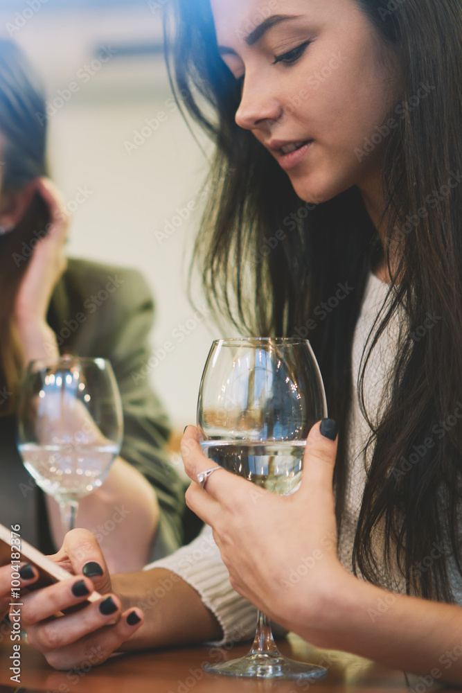 Caucasian millennial women socialising online and ignoring live communication during wine time with friends, beautiful hipster girls chatting online via modern cellular gadgets connected to wireless Caucasian millennial women socialising online and ignoring live communication during wine time with friends, beautiful hipster girls chatting online via modern cellular gadgets connected to wireless