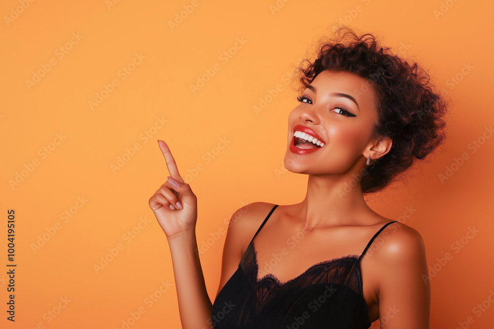 Obraz premium Beautiful girl posing on orange background and pointing finger at place for advertisement and text