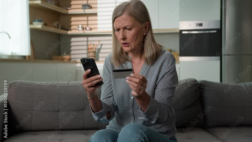 Angry confused senior Caucasian woman mature elderly female mother hold credit card security problem using bank app for payment retired grandparent mobile phone scam money loss failure error home sofa