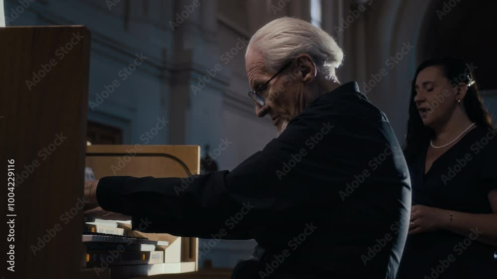 Zoom in shot of senior man playing church organ and accompanying female vocalist singing behind him