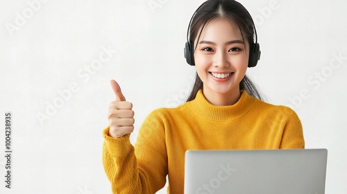 A woman wearing headphones is giving a thumbs up while sitting at a desk with a laptop. Concept of positivity and productivity, as the woman is enjoying her work or task photo