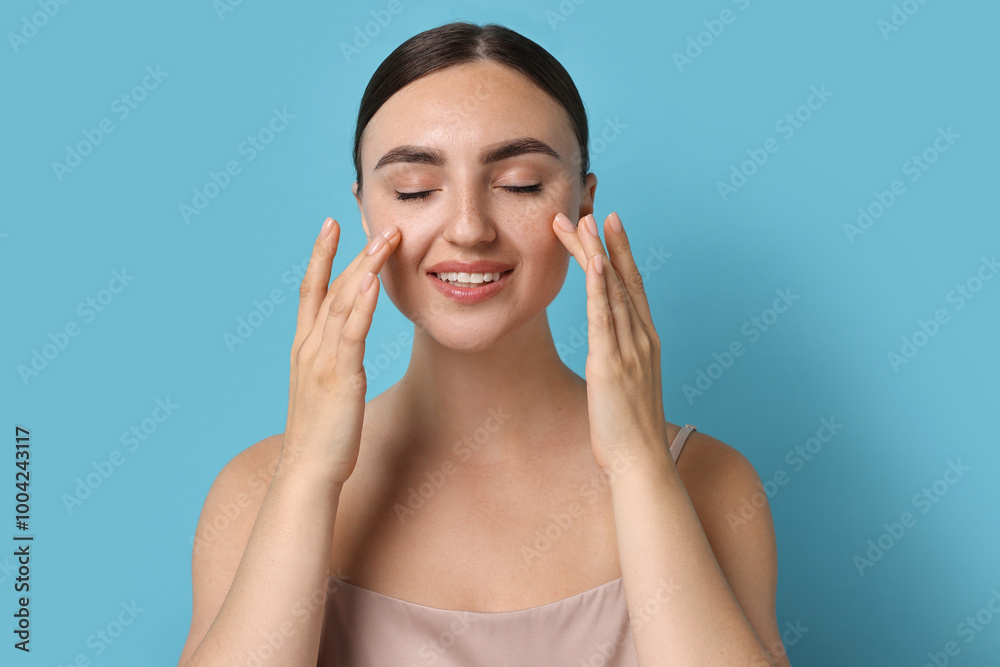 Beautiful young woman doing facial massage on light blue background Beautiful young woman doing facial massage on light blue background