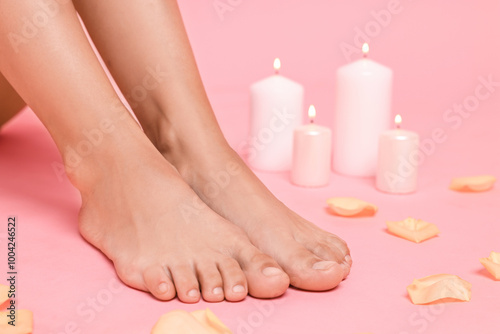 Woman with smooth feet, burning candles and petals on pink background, closeup