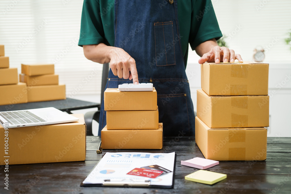 A man is working at his desk, preparing parcel boxes for shipment. He checks and packs items carefully, using shockproof materials, and attaches labels before sending them to customers via EMS. A man is working at his desk, preparing parcel boxes for shipment. He checks and packs items carefully, using shockproof materials, and attaches labels before sending them to customers via EMS.