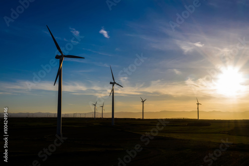 Silhouette Modern windmills with propellers standing in rural farmland agri meadow over orange sunset sky. Wind blowing generating renewable energy for clean resources. Electric power production photo