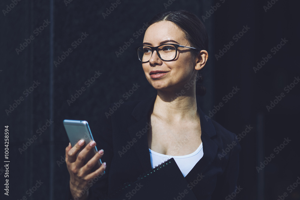 Smiling business woman in eyewear for vision correction holding mobile phone in hand using 4g connection for communicate with partners via application, concept of professionalism and technology Smiling business woman in eyewear for vision correction holding mobile phone in hand using 4g connection for communicate with partners via application, concept of professionalism and technology