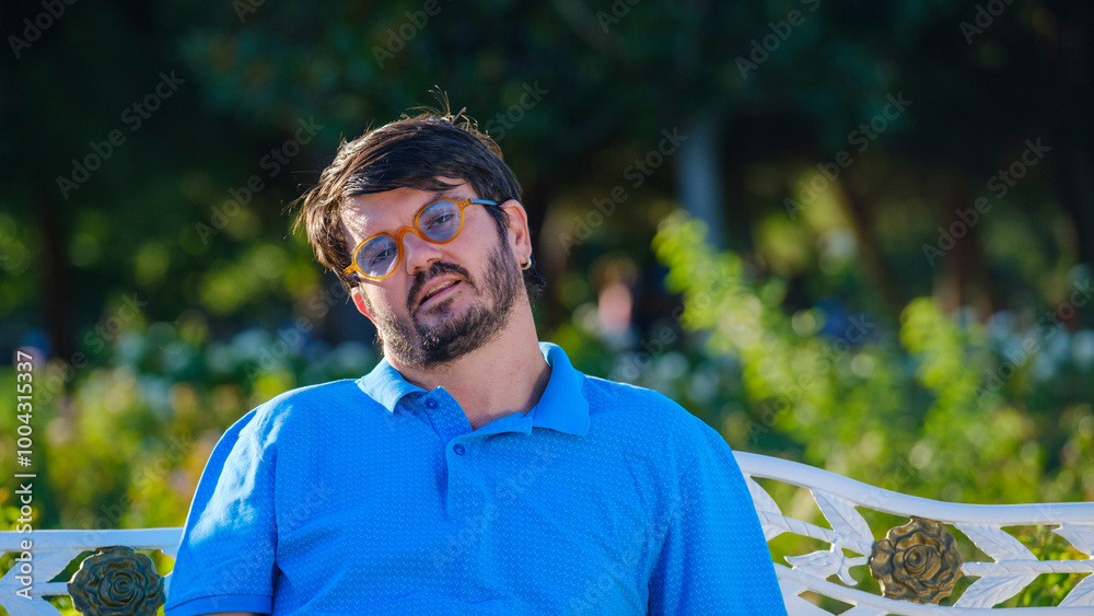 A middle-aged businessman is sitting on a bench in a tree-filled park on a sunny summer day, posing while enjoying the pleasant weather A middle-aged businessman is sitting on a bench in a tree-filled park on a sunny summer day, posing while enjoying the pleasant weather