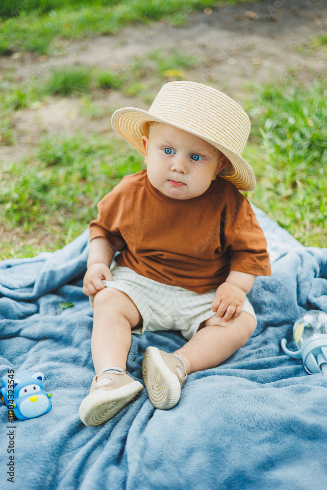 A little boy is sitting in the grass outdoors in the park with a hat and smiling. The child is sitting in the park on the grass. A boy in a straw hat. A little boy is sitting in the grass outdoors in the park with a hat and smiling. The child is sitting in the park on the grass. A boy in a straw hat.