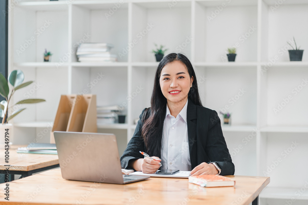 professional woman sits at desk in modern office, smiling confidently while working on laptop. bright workspace features plants and organized shelves, creating productive atmosphere. professional woman sits at desk in modern office, smiling confidently while working on laptop. bright workspace features plants and organized shelves, creating productive atmosphere.