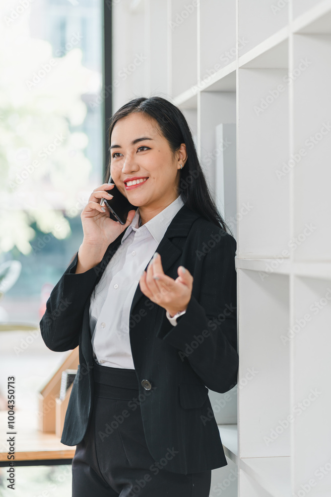 professional woman in black suit smiles while talking on her phone, exuding confidence and positivity in modern office setting. professional woman in black suit smiles while talking on her phone, exuding confidence and positivity in modern office setting.
