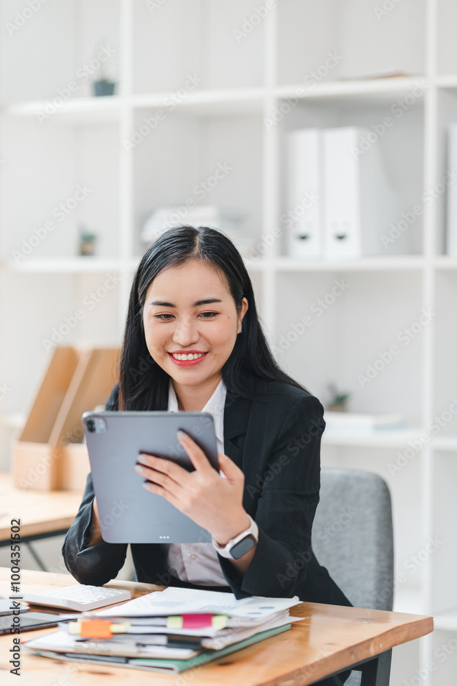 young woman in black suit smiles while using tablet in modern office setting, surrounded by organized paperwork and clean workspace. Her expression conveys happiness and engagement. young woman in black suit smiles while using tablet in modern office setting, surrounded by organized paperwork and clean workspace. Her expression conveys happiness and engagement.