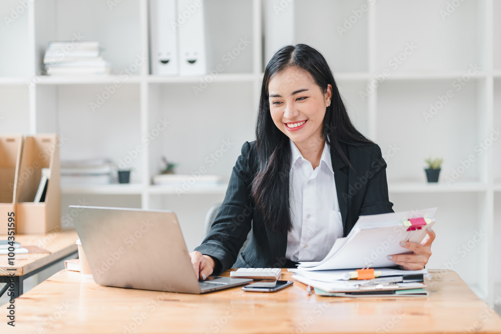 professional woman is working at her desk, smiling while using laptop and organizing documents. bright office environment enhances her positive energy and productivity. professional woman is working at her desk, smiling while using laptop and organizing documents. bright office environment enhances her positive energy and productivity.