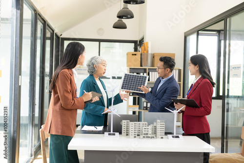 Engineers meeting about wind turbine model and house model. Renewable energy and housing development concept. Team of architects and engineers in modern office discussing design structure.