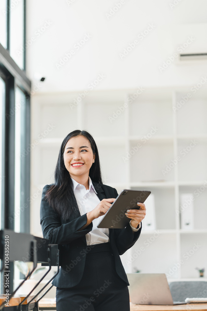 professional woman in black suit smiles while holding tablet in modern office setting. bright, airy space features large windows and minimalist decor, creating inviting atmosphere. professional woman in black suit smiles while holding tablet in modern office setting. bright, airy space features large windows and minimalist decor, creating inviting atmosphere.