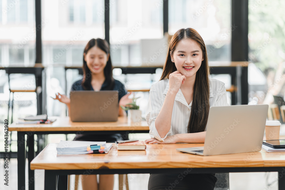 professional woman smiles confidently while working on her laptop in modern office environment, with colleague in background engaged in her tasks. atmosphere is productive and collaborative. professional woman smiles confidently while working on her laptop in modern office environment, with colleague in background engaged in her tasks. atmosphere is productive and collaborative.