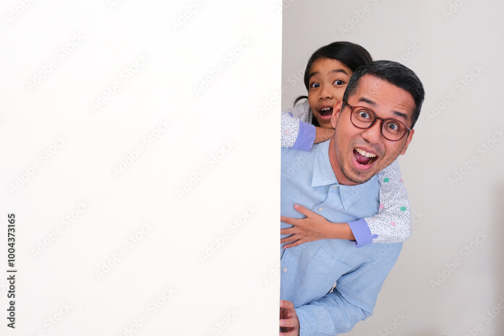 A father and his daughter peeking from behind billboard with amazed expression