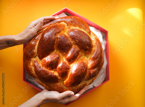 Hands holding round fresh challah in a Magen David shaped box on a yellow background. Jewish New Year. Traditional aromatic pastries for the holiday