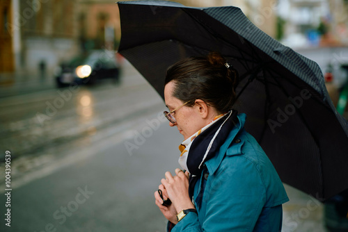 Side profile of an adult with a black umbrella on a rainy city street. photo