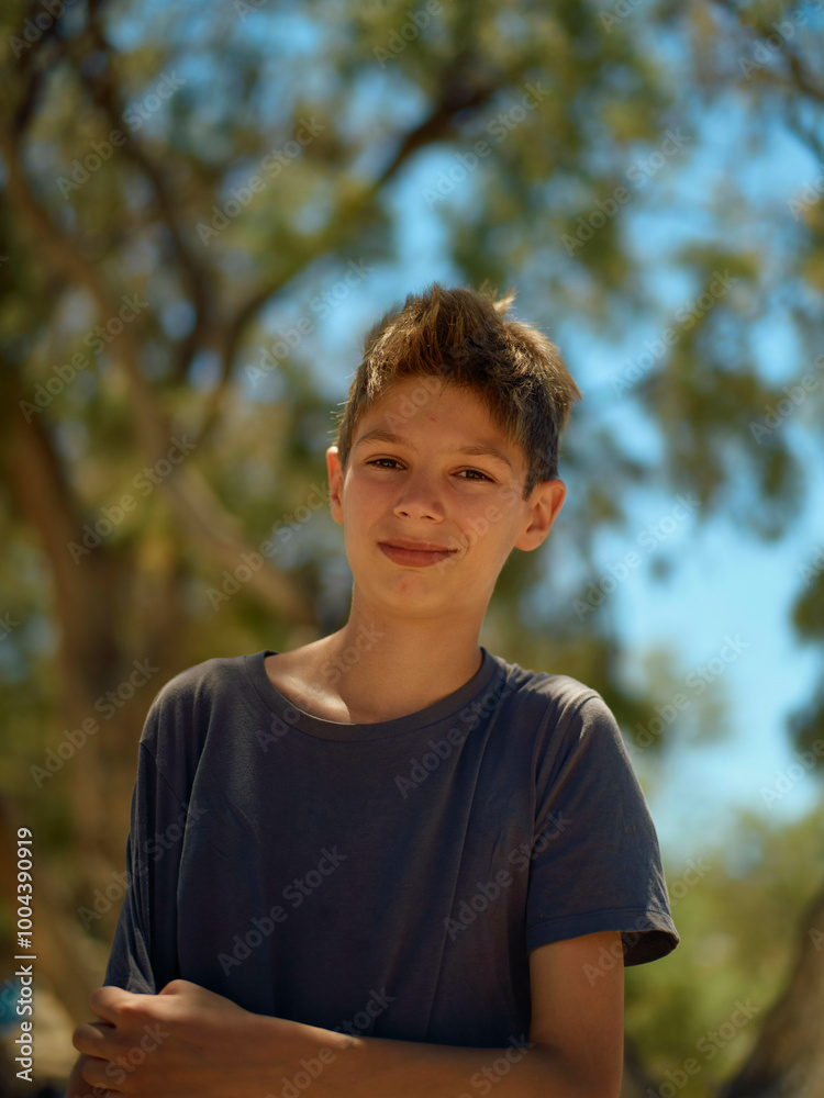 A smiling boy in a blue t-shirt stands outdoors with trees in the background. A smiling boy in a blue t-shirt stands outdoors with trees in the background.