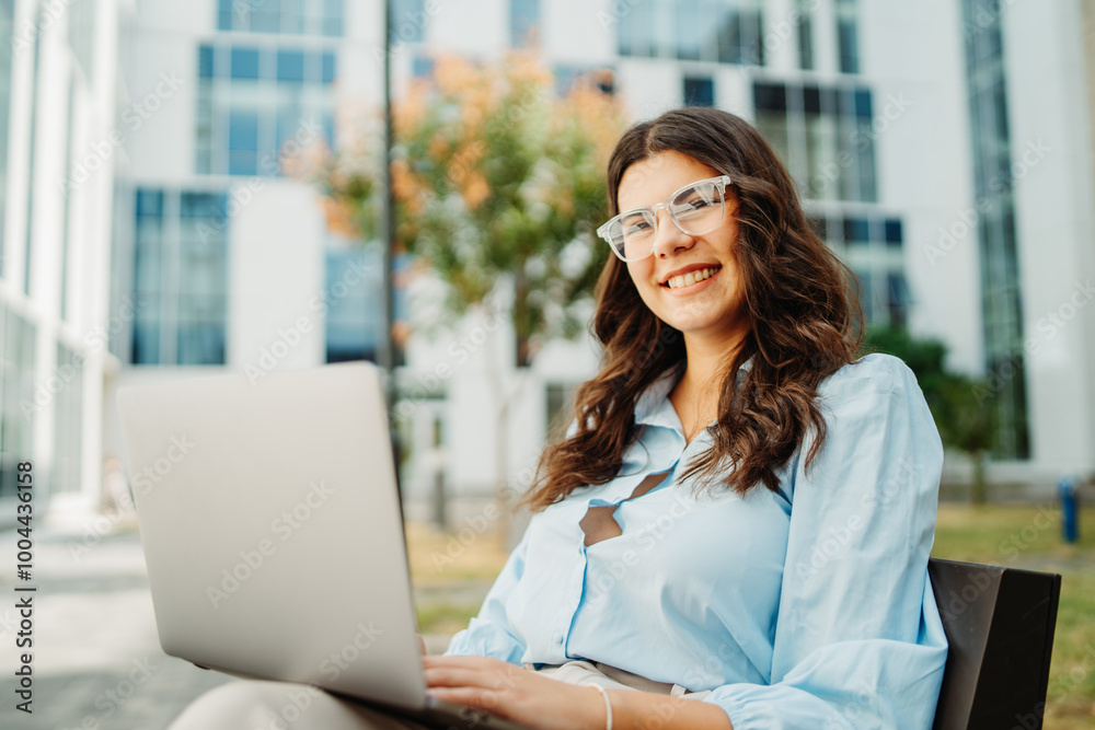 Young businesswoman is working on laptop in front of modern building	